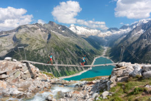 two runners on the tibetan bridge near Olperer hut with Schlegeis Stausee on the background, Zillertal Alps, Tyrol, Schwaz district, Austria. two runners on the tibetan bridge near Olperer hut with Schlegeis Stausee on the background, Zillertal Alps, Tyrol, Schwaz district, Austria.